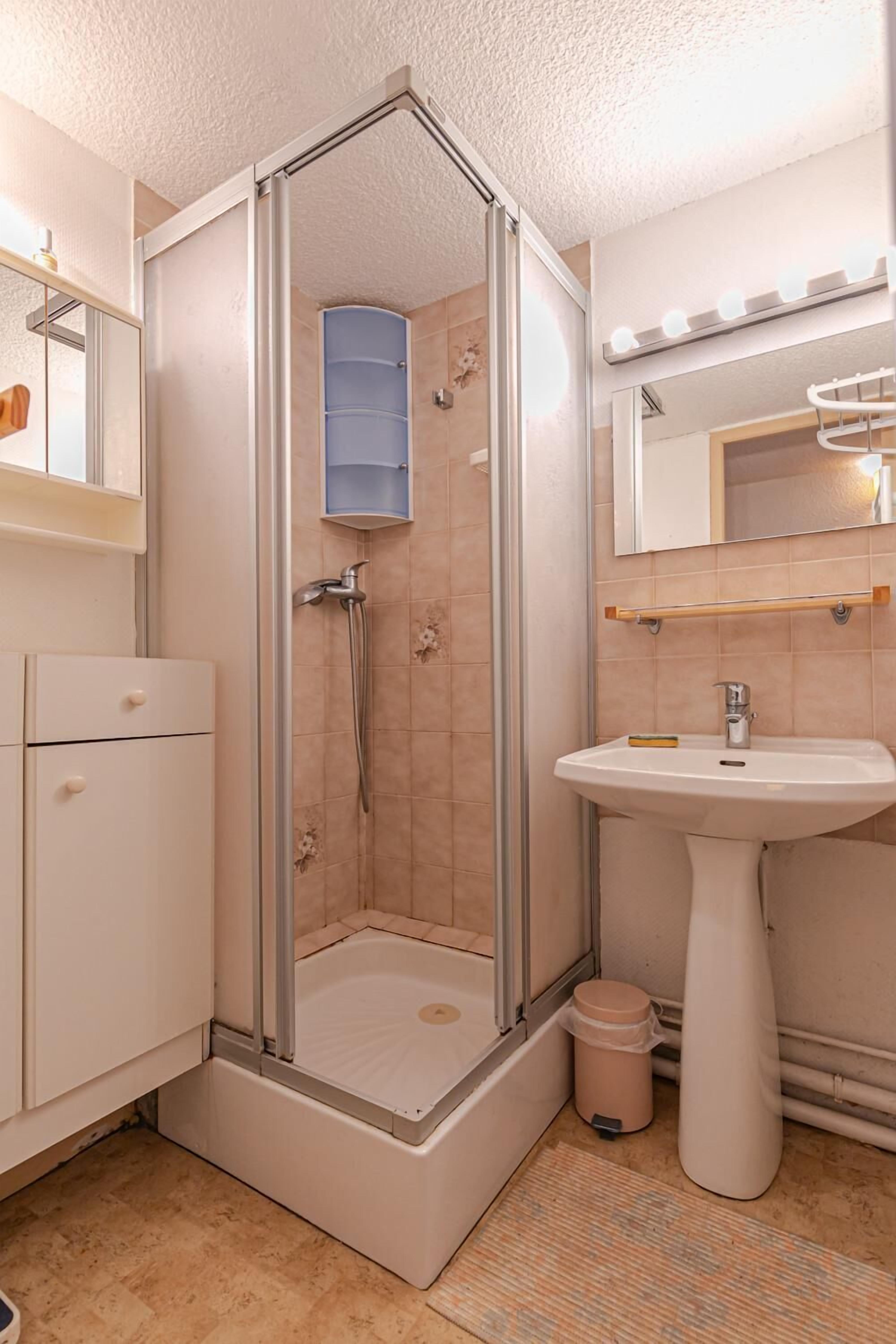 A modern bathroom with a glass-enclosed shower, a pedestal sink, and a vanity with drawers.