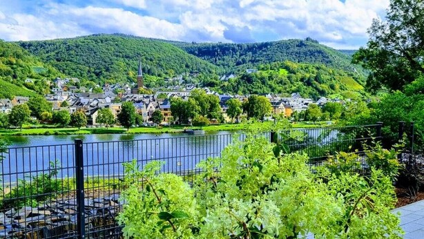 A riverside walkway with a view of a town and hills in the background.