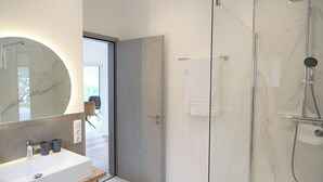 A modern bathroom with a large mirror, a sink, and a glass-enclosed shower.