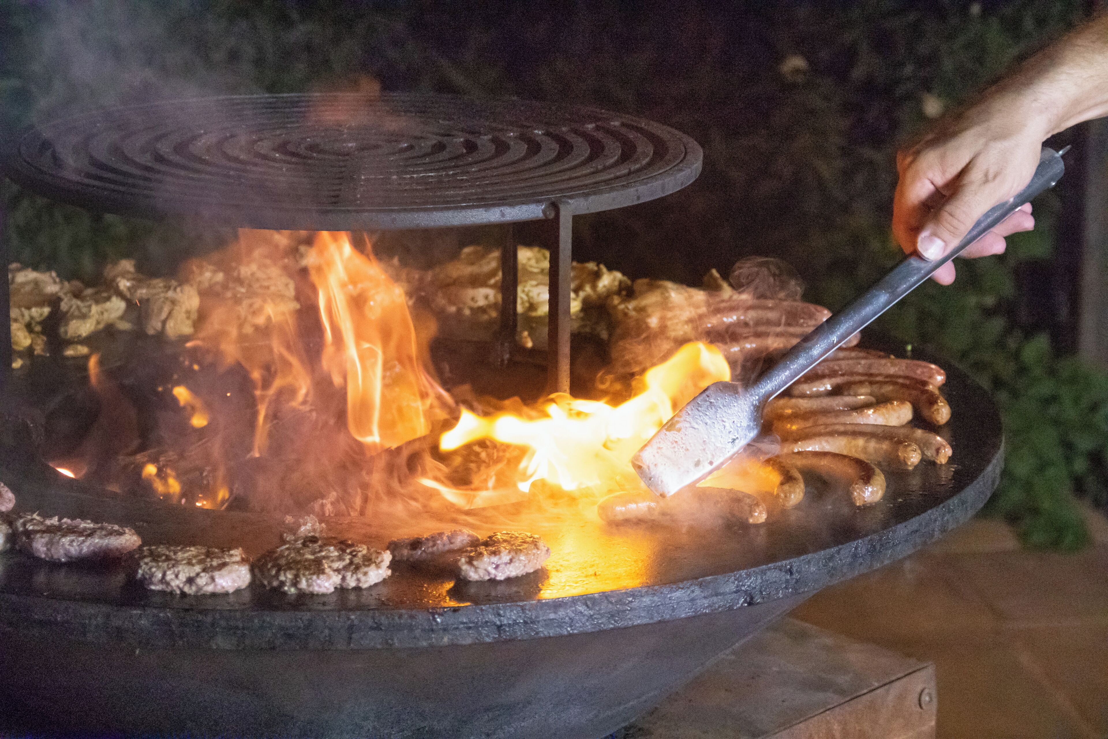 Een barbecue met worstjes die boven een open vuur worden gebakken.