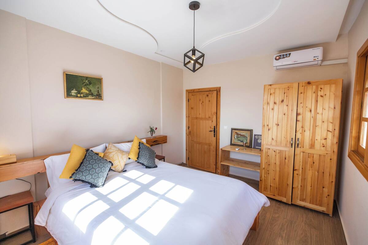 A bedroom with a bed, wooden wardrobe, and a wall-mounted air conditioner.