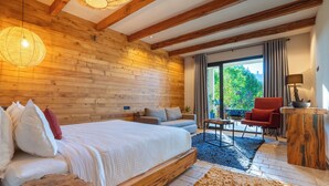 A bedroom with a wooden ceiling, a bed, a sofa, a red chair, a small table, and a view of greenery outside. - Bio et bois - Luxury Bio farm (Ain Chkef)