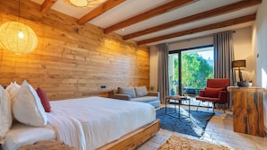 A bedroom with a wooden ceiling, a bed, a sofa, a red chair, a small table, and a view of greenery outside. - Bio et bois - Luxury Bio farm (Ain Chkef)