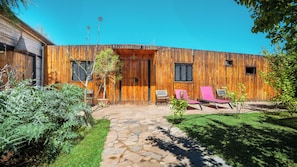 A wooden building with a stone pathway leading to a door, a bench, and two pink chairs.