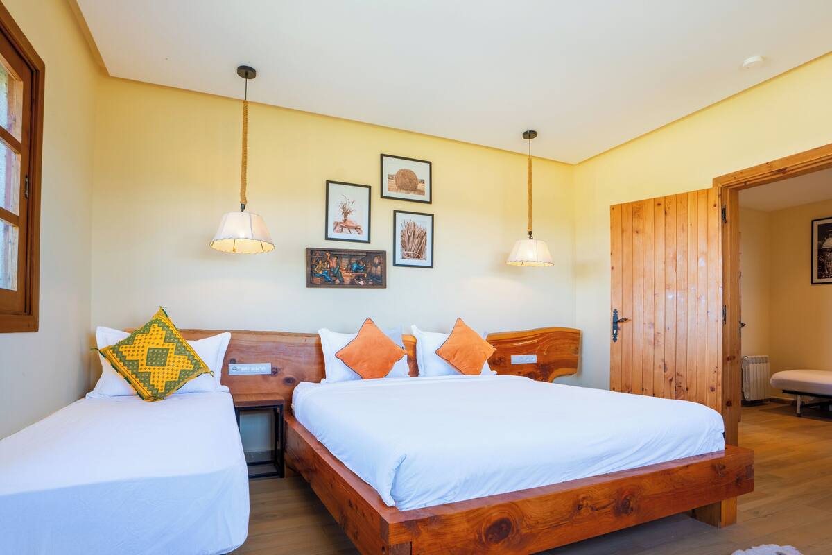 A bedroom with two beds, wooden headboards, a wooden door, and a window with a view.