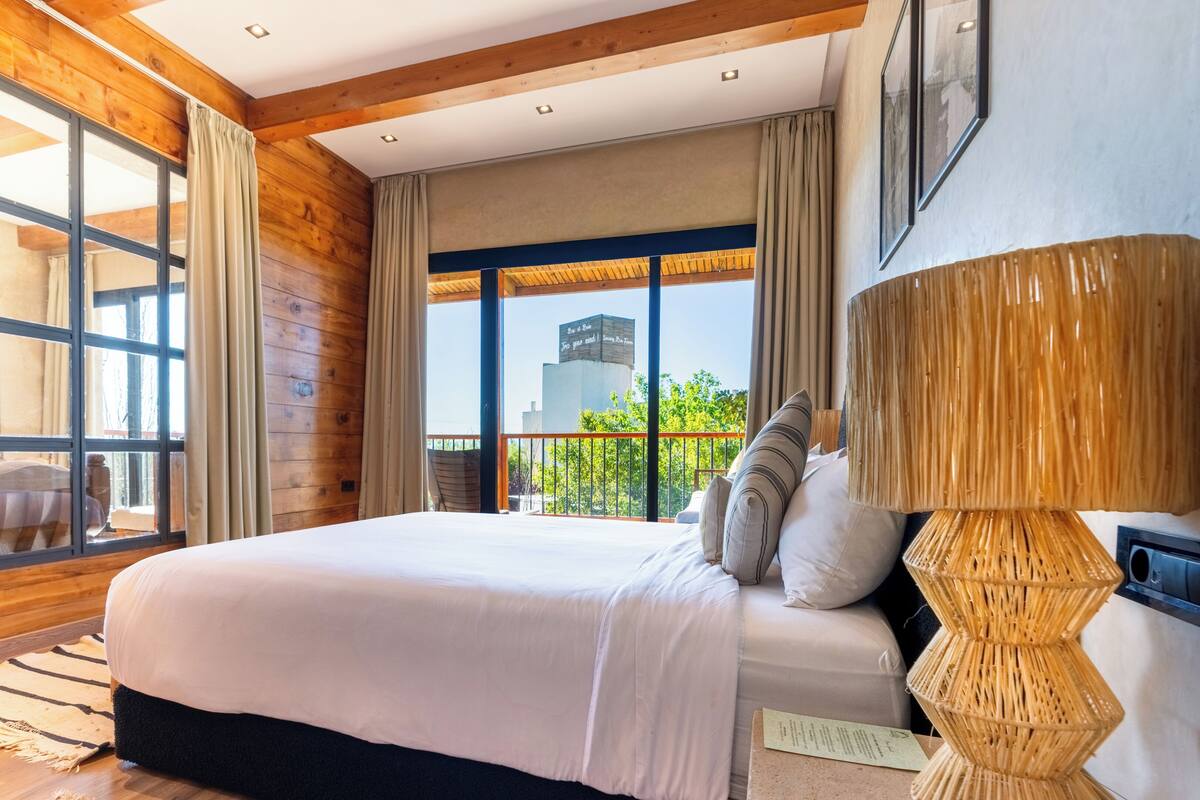 A bedroom with a large bed, wooden walls, a balcony with a view, and a modern lamp.