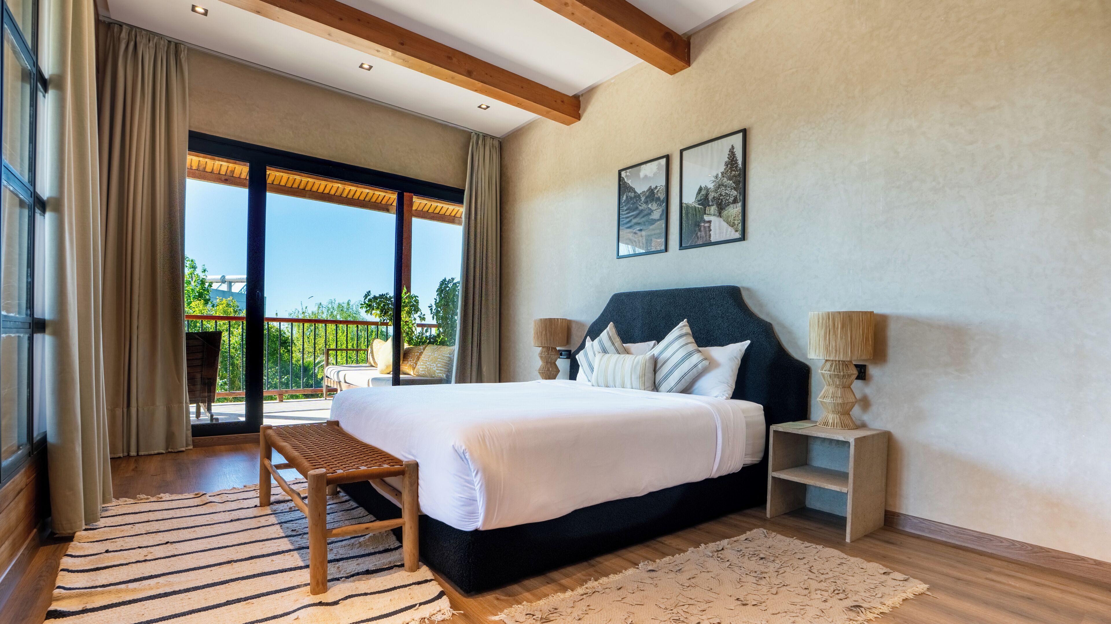 Quarto com uma cama grande, um banco de madeira, duas mesas de cabeceira e vista para o verde através de uma porta deslizante.