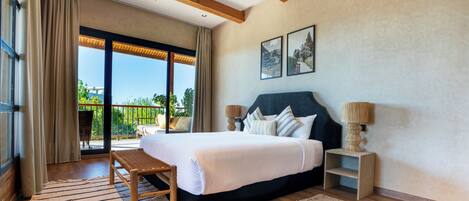 Quarto com uma cama grande, um banco de madeira, duas mesas de cabeceira e vista para o verde através de uma porta deslizante.