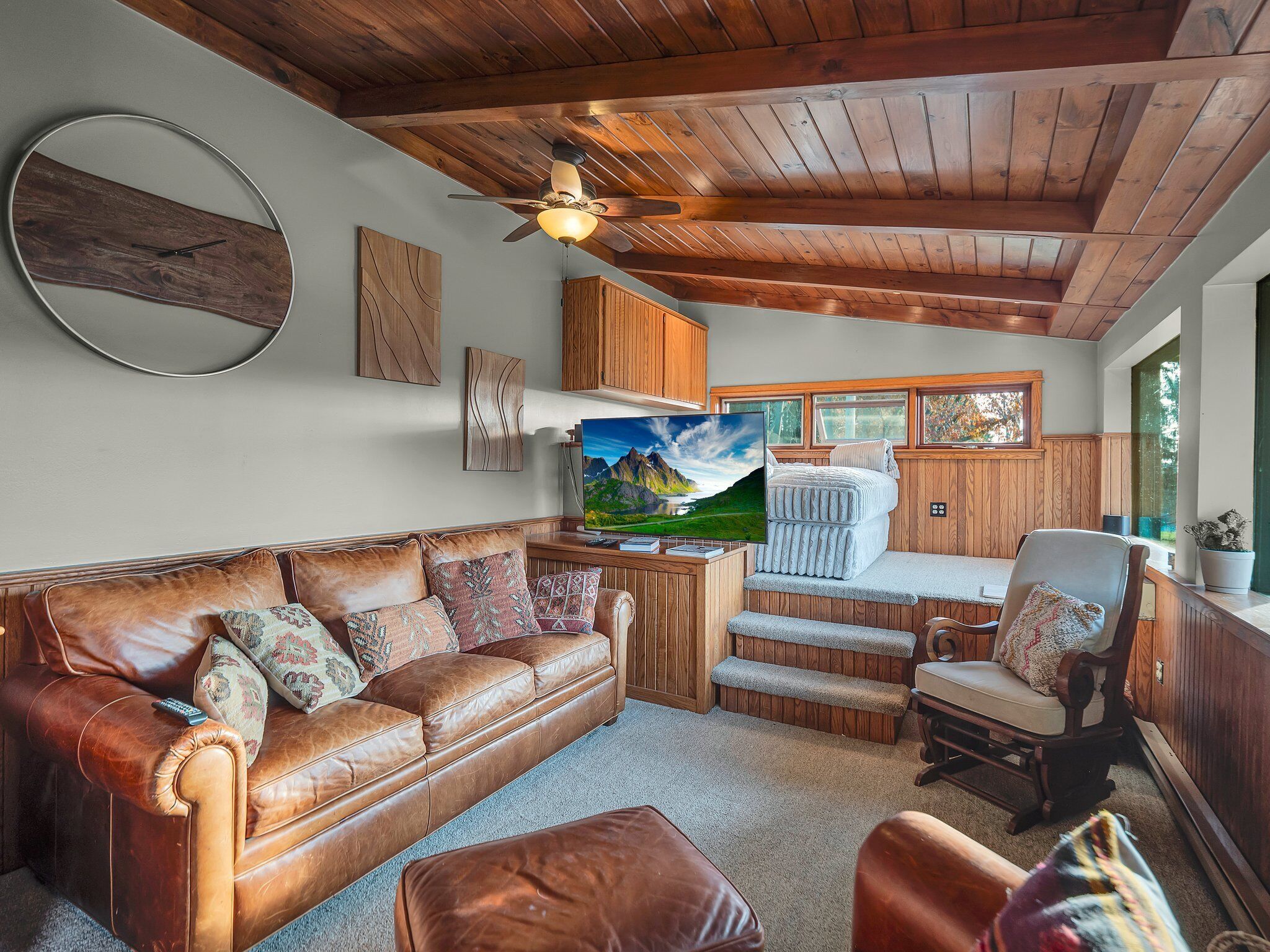 A cozy living room with a leather sofa, a wooden ceiling, and a large window.