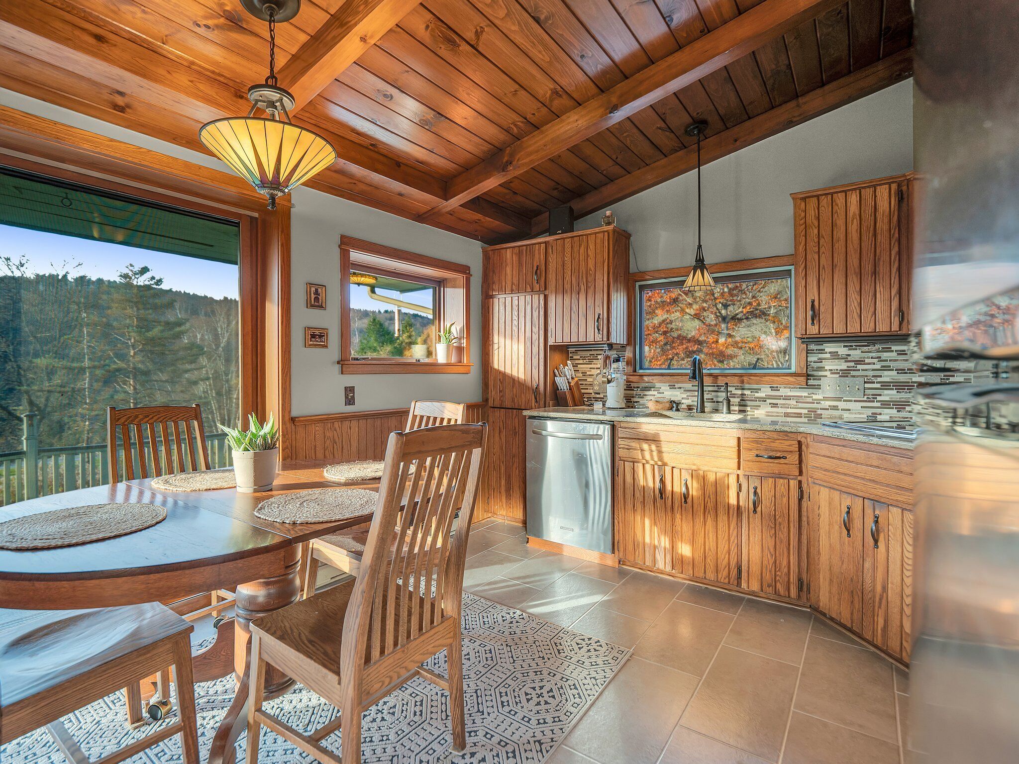 A modern kitchen with wooden cabinets, a built-in island, and a large window overlooking a forested area.