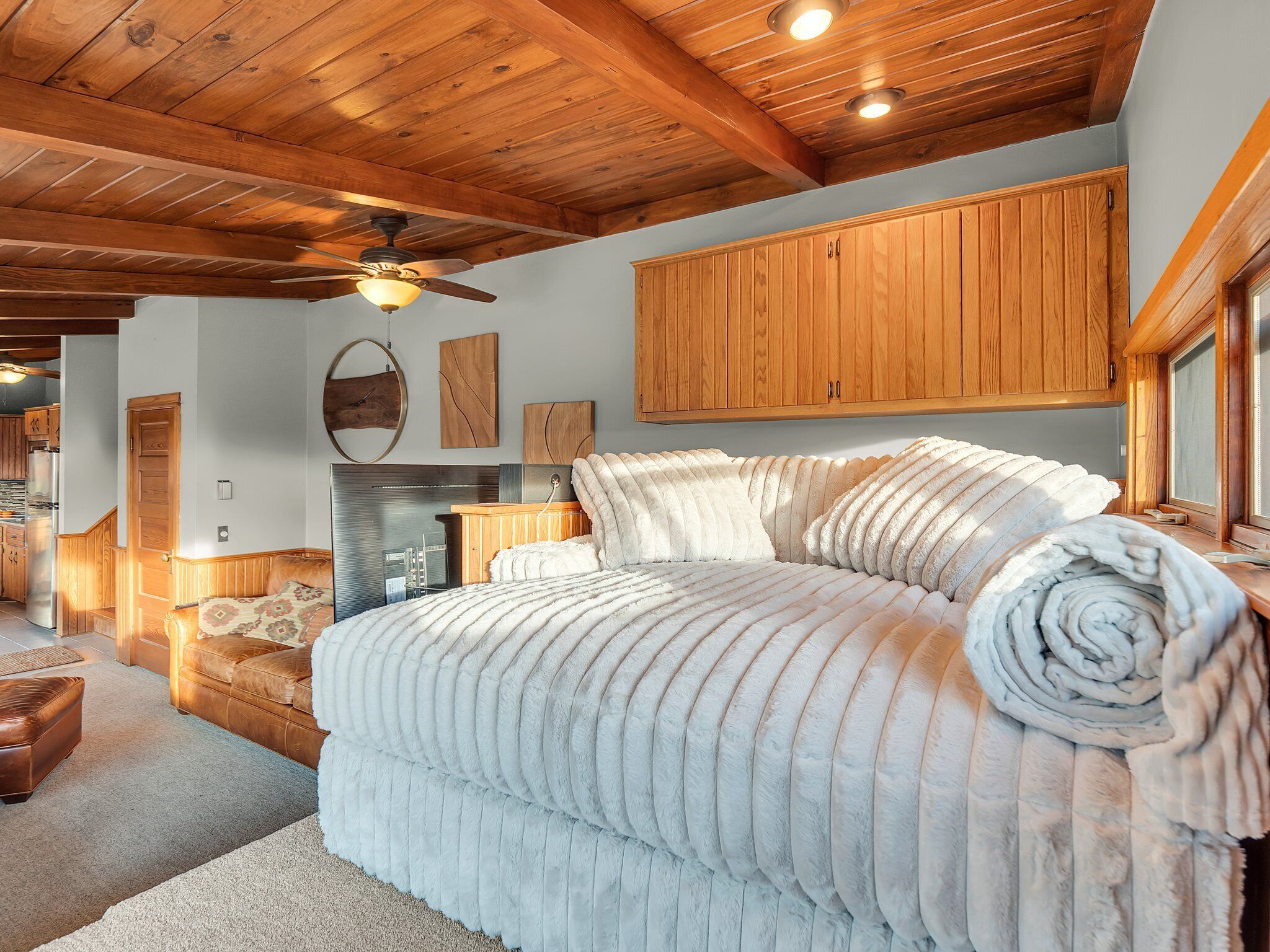 A bedroom with a large bed, wooden ceiling beams, a ceiling fan, and a wooden cabinet above the bed.