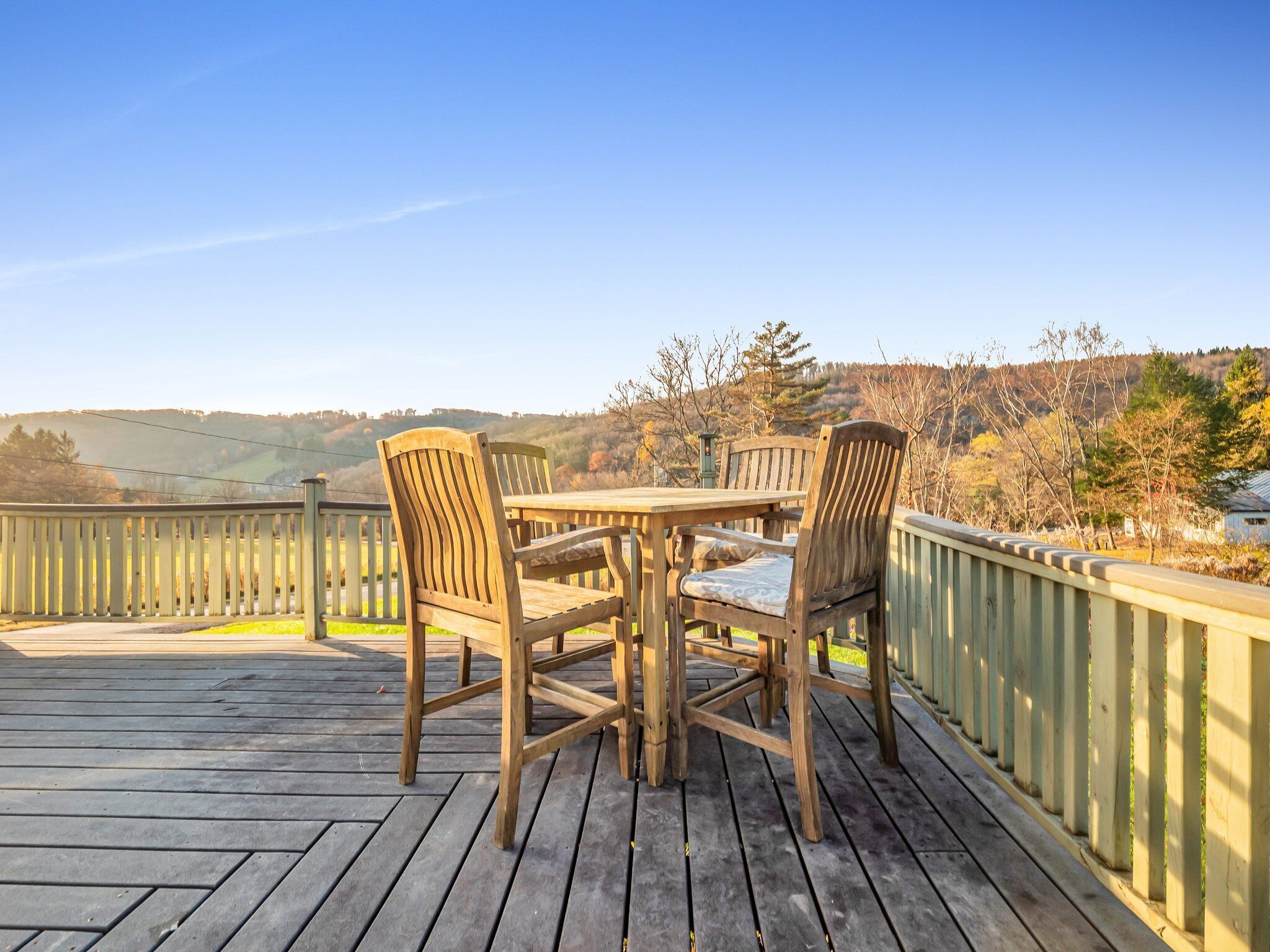 Een houten terras met tafel en stoelen, met uitzicht op een pittoresk landschap met heuvels en bomen.