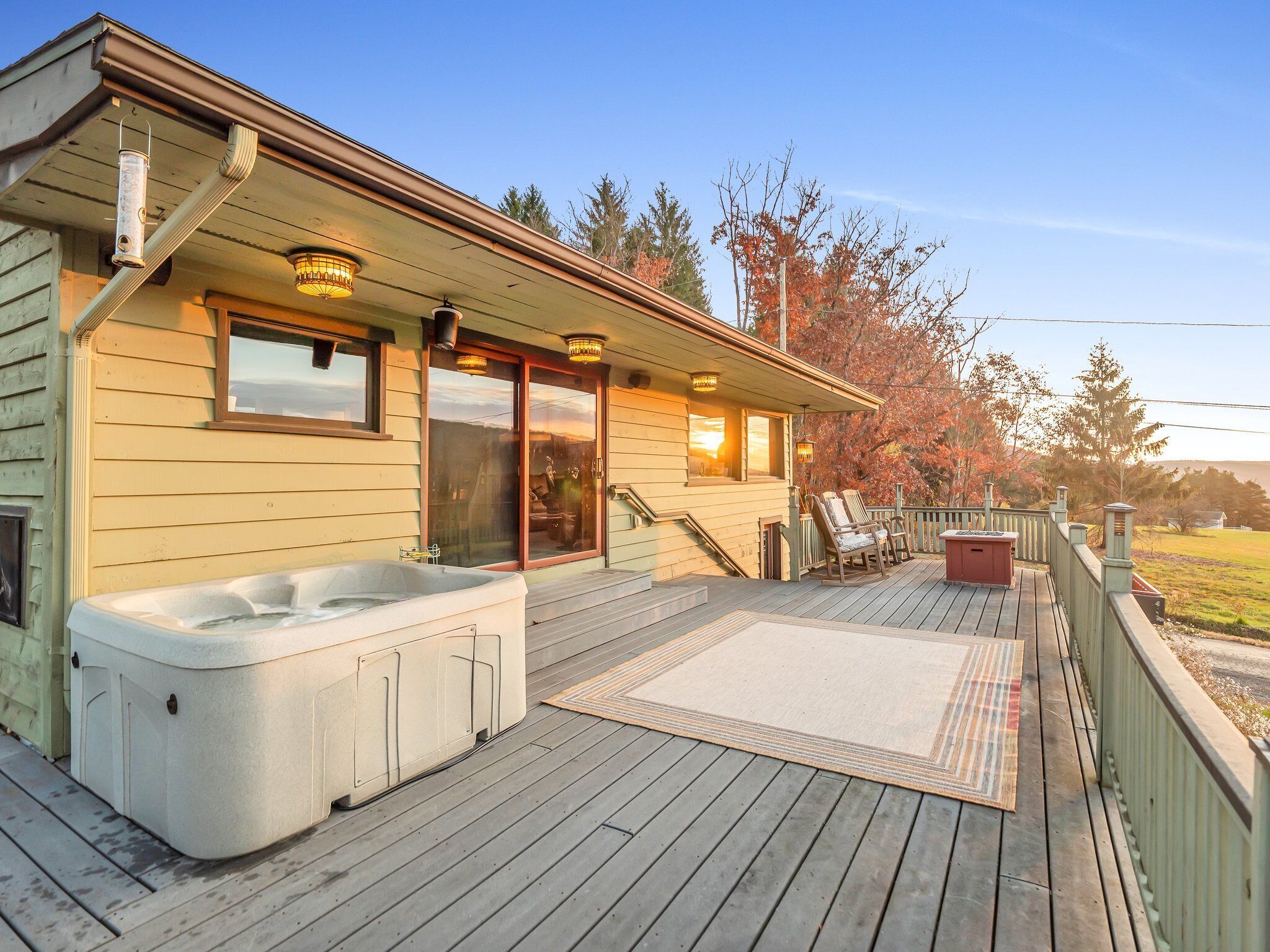 Una terraza de madera con un jacuzzi, asientos exteriores y vistas a árboles.