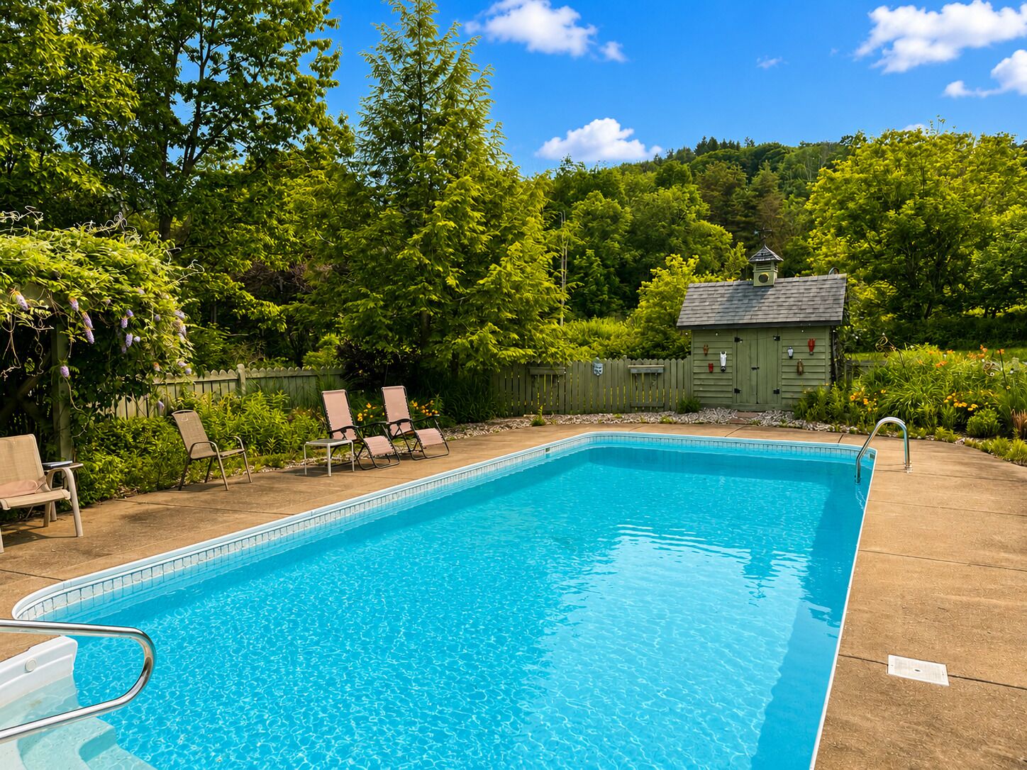 Ein rechteckiger Pool mit einer Metallleiter, umgeben von einer Holzterrasse. Im Hintergrund sind Liegestühle und eine kleine Gartenhütte zu sehen.