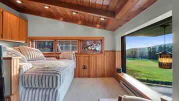 A bedroom with a large bed, wooden ceiling, and a view of a green landscape through a large window.