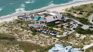 Vista aérea de un complejo turístico frente al mar, con piscina, acceso a la playa y aparcamiento.