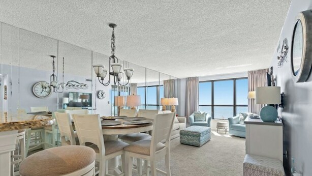 A modern hotel room with a dining area, a living area with a view, and a kitchenette. - Windemere 605 -Oceanfront 3BR/2BA-Indoor Pool (North Myrtle Beach)