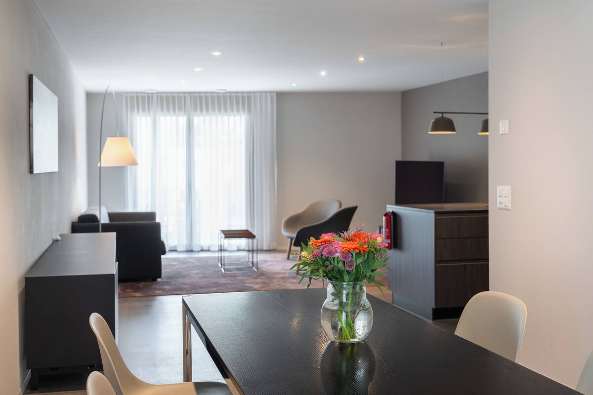 A modern hotel room with a dining area, a living space, and a kitchen.