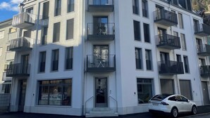 A modern multi-story building with balconies, a car parked in front, and a clear sky. - Modern City Apartments (Interlaken)