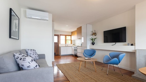 A modern living room with a grey sofa, two blue chairs, a coffee table, and a flat-screen TV mounted on the wall. - 2-bed apartment in the heart of Ponsonby (Auckland)