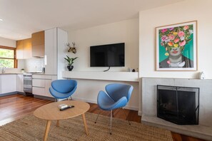 A modern living room with a fireplace, a flat-screen TV, and two blue chairs.