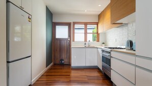 A narrow kitchen with wooden flooring, white cabinets, a stainless steel stove, and a view through a window. - 2-bed apartment in the heart of Ponsonby (Auckland)