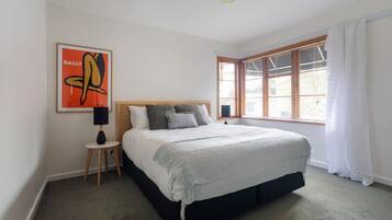 A bedroom with a bed, a nightstand, a lamp, a window with blinds, and a framed artwork on the wall.