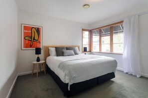A bedroom with a bed, a nightstand, a lamp, a window with blinds, and a framed artwork on the wall.