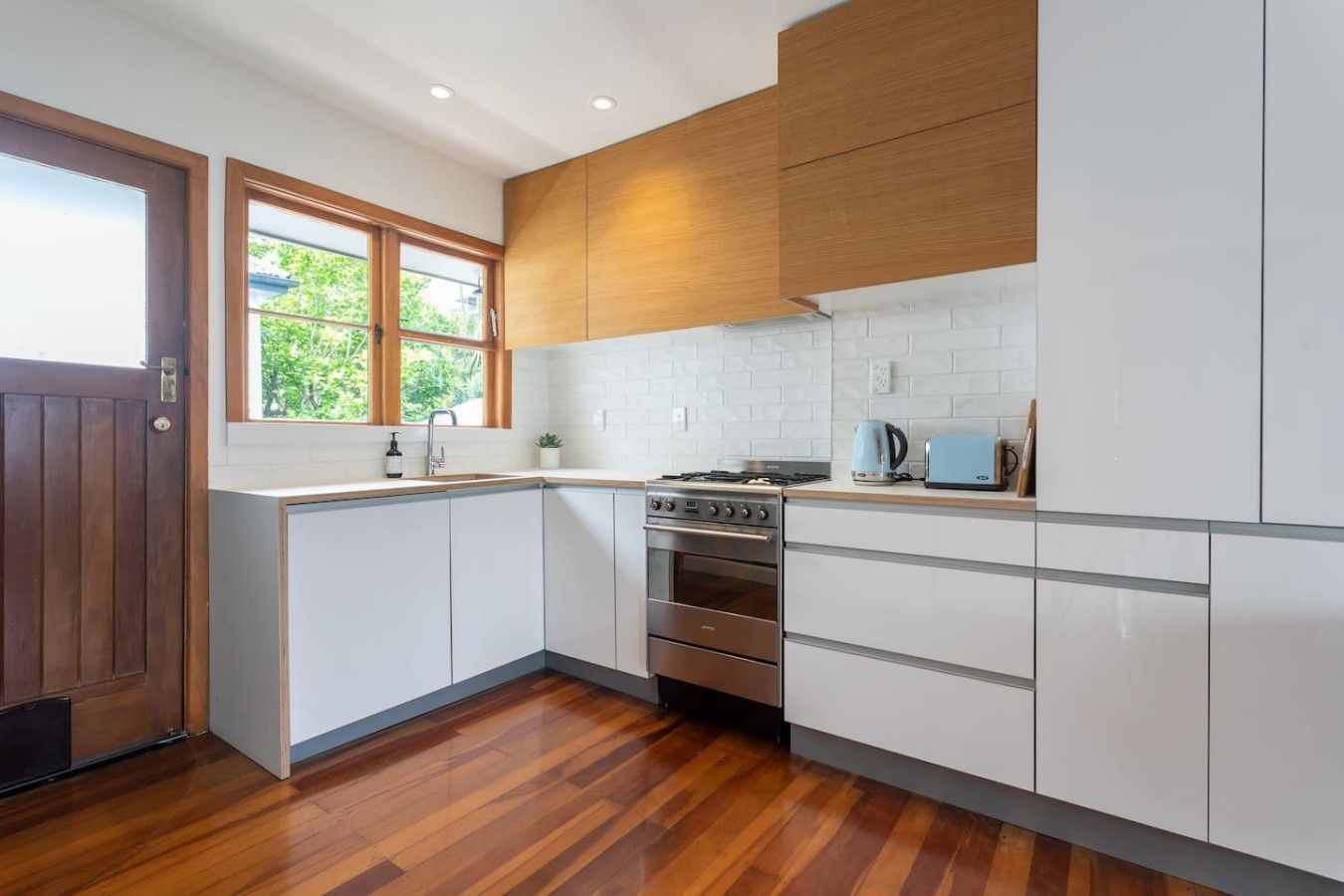 A modern kitchen with white cabinets, a wooden door, and a window.