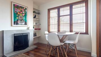 A dining area with a fireplace, white chairs, and a window with blinds.