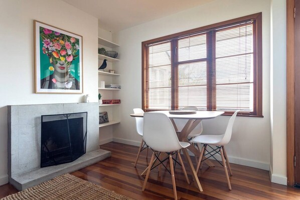 A dining area with a fireplace, white chairs, and a window with blinds.