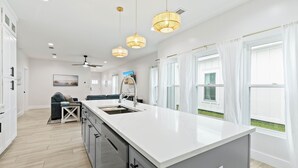 A modern kitchen with a large island, pendant lights, and a view of the outdoors. - Family home near OWA, beaches. King bed, cornhole, fire pit, pet friendly! (Foley)