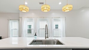 A modern kitchen with a large island, stainless steel sink, and three hanging pendant lights. - Family home near OWA, beaches. King bed, cornhole, fire pit, pet friendly! (Foley)