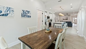A modern kitchen with white cabinets, a microwave, and a dining area with a wooden table and white chairs. - Family home near OWA, beaches. King bed, cornhole, fire pit, pet friendly! (Foley)