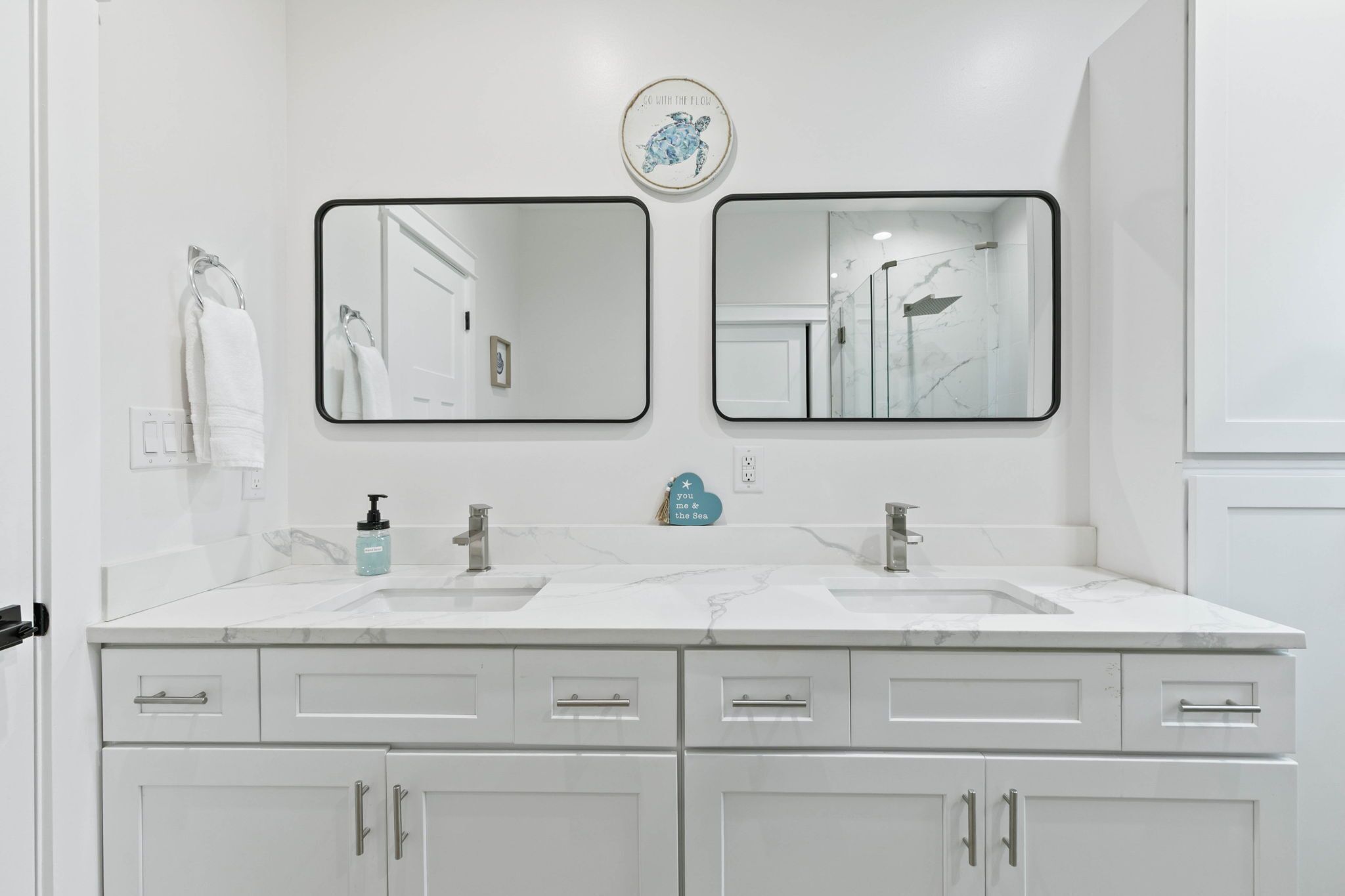 Une salle de bain avec deux lavabos, un porte-serviettes, un distributeur de savon et un objet décoratif accroché au mur.
