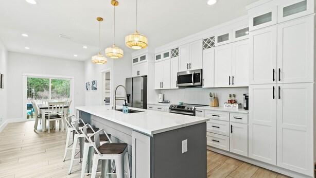 A modern kitchen with white cabinets, a central island with bar stools, and pendant lighting. - Family home near OWA, beaches. King bed, cornhole, fire pit, pet friendly! (Foley)