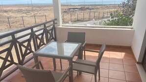 A balcony with a table and chairs, overlooking a barren landscape with a fence and some greenery. - Tortuga/3beds/pool/tv/wifi (Sal)