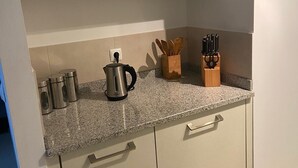 A kitchen with white cabinets, a granite countertop, stainless steel containers, a kettle, wooden utensils, and a knife block. - Tortuga/3beds/pool/tv/wifi (Sal)