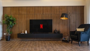 A modern living room with a large flat-screen TV mounted on a wooden wall, a black armchair, a floor lamp, and a potted plant. - Prime Select Old Cairo Nile View (Cairo)