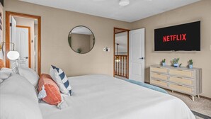 Une chambre à coucher comprenant un lit, un téléviseur fixé au mur, un ventilateur de plafond, un miroir et une commode avec des tiroirs.