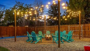 Un jardin avec un foyer, des fauteuils Adirondack verts et des guirlandes lumineuses.