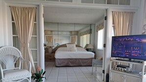 A hotel room with a large bed, a television, a wicker chair, and a small table with a lamp.