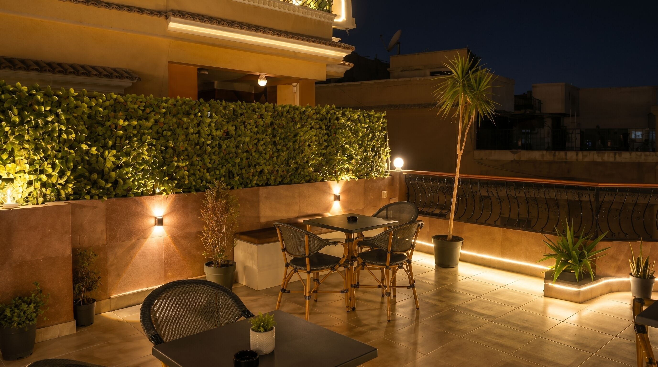 A rooftop patio with a table and chairs, potted plants, and a wall of greenery.
