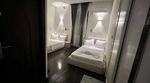 A hotel room with two beds, a small seating area, a ceiling light, and a wall-mounted air conditioner.