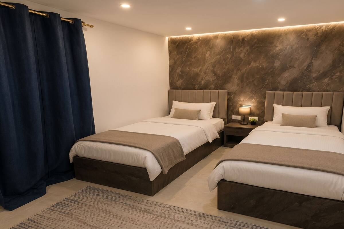 A double room with two beds, a dark curtain, a marble wall, and a small bedside table with a lamp.