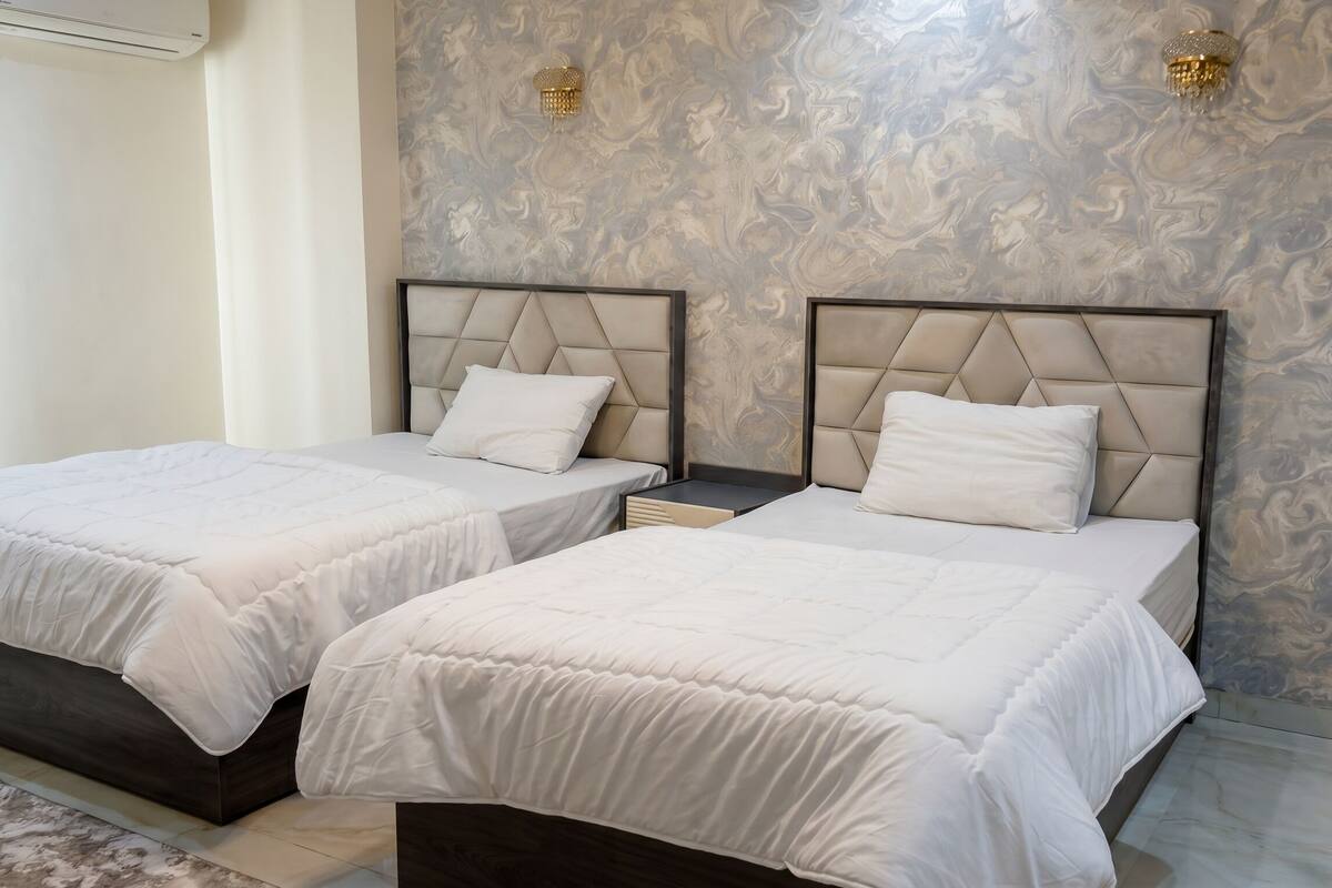 Two beds with headboards, a nightstand, a marble-patterned wall, and a ceiling-mounted air conditioning unit.