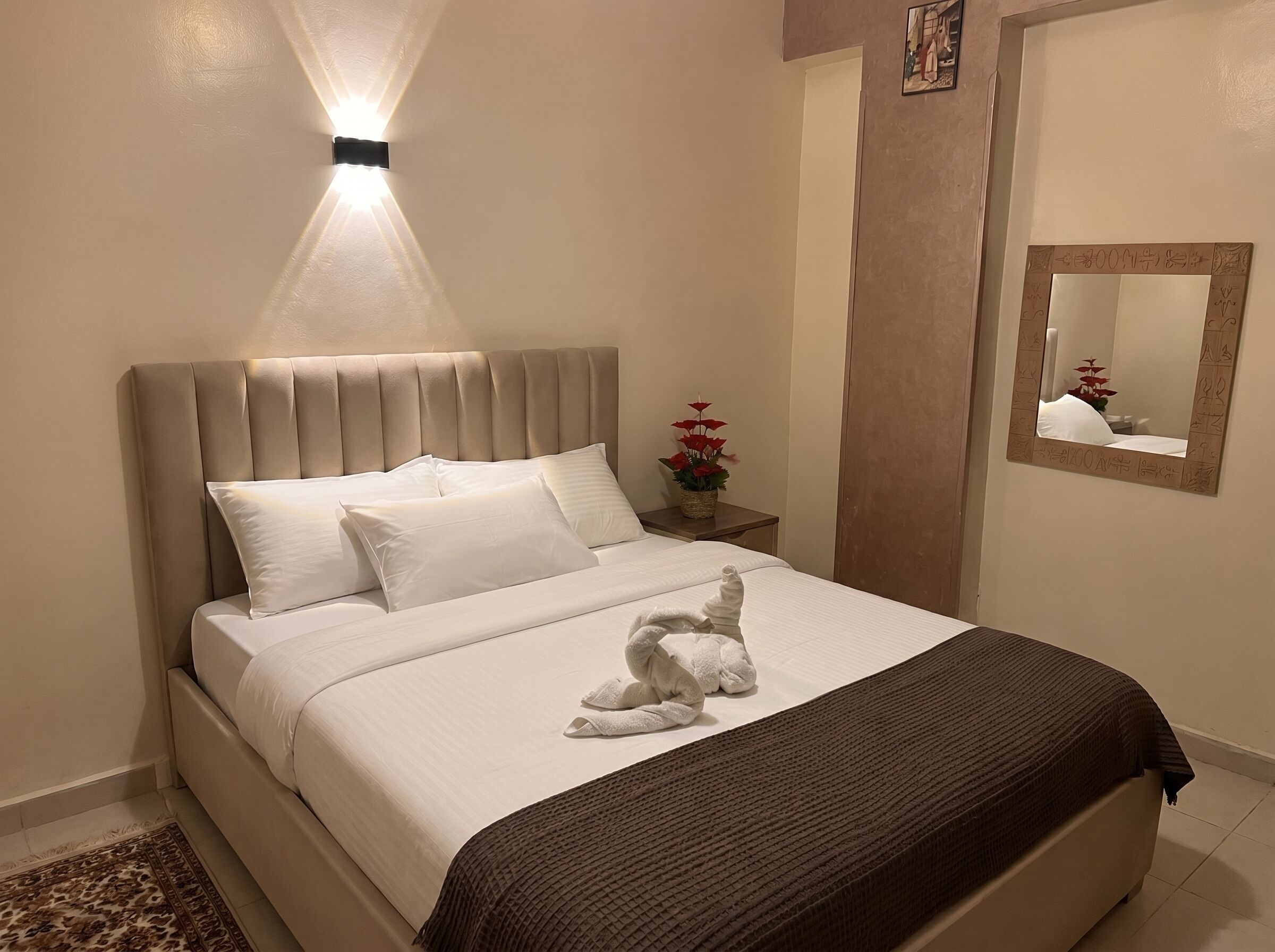 A bed with a headboard, a bedside table with a plant, and a mirror on the wall.