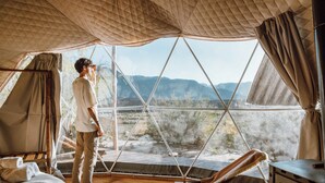 Ein Zeltraum mit Bett, Stuhl und Blick auf eine gebirgige Landschaft.