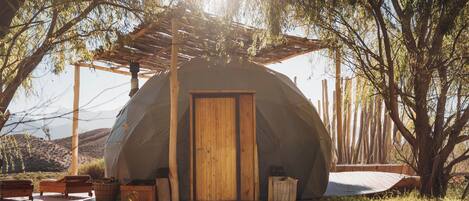 A dome-shaped tent with a wooden door, a wooden bench, and a small table on a wooden deck.