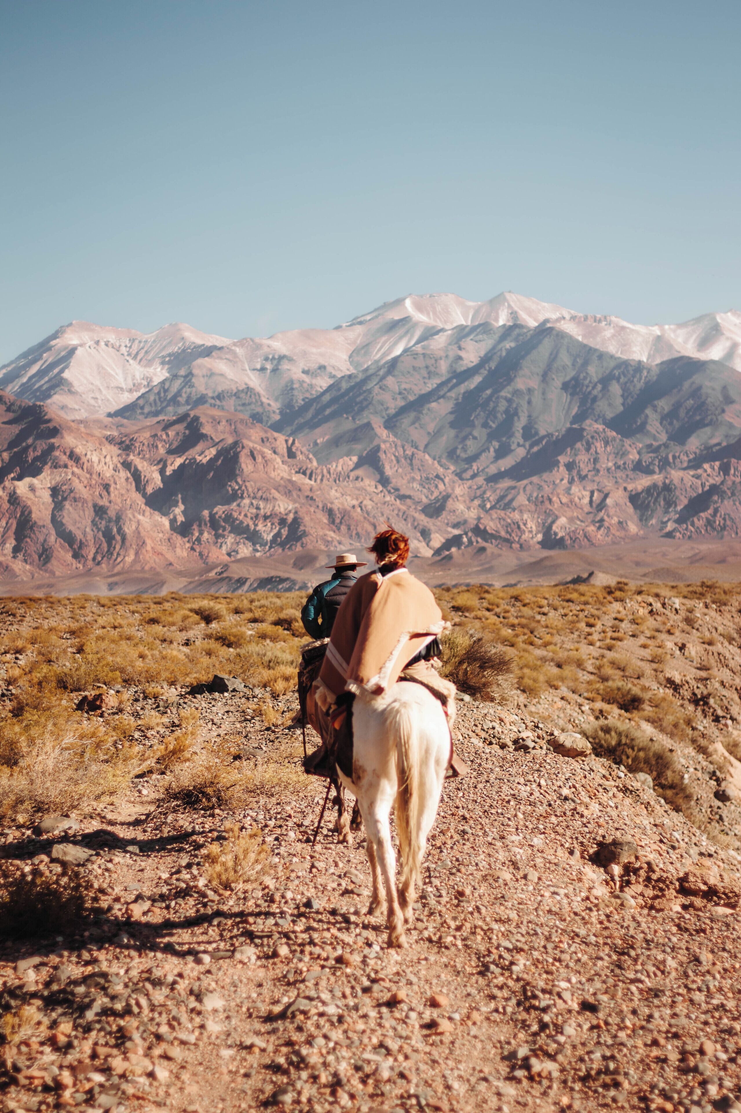 Une personne à cheval, évoluant sur un terrain rocheux, avec des montagnes en arrière-plan.